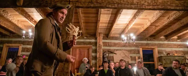 A costumed interpreter speaking to a candlelit crowd inside a log building