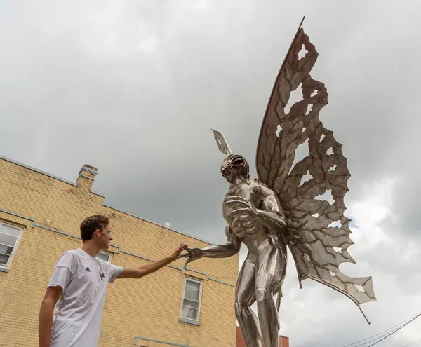 A visitor reaching up to touch the stainless-steel Mothman statue
